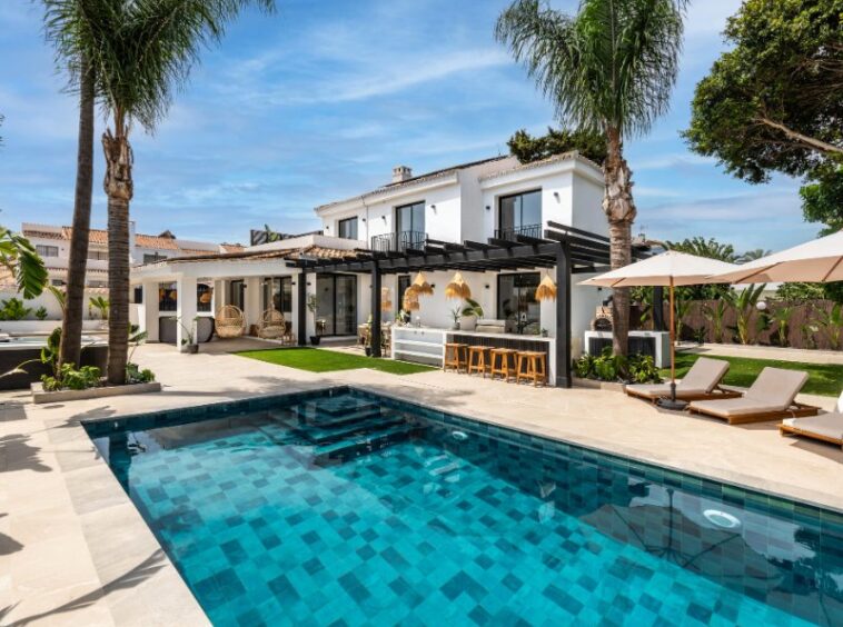 Charming facade of a cozy beach villa, just steps from the sea, showcasing a modern yet relaxed architectural design, with large windows, a welcoming entrance, and a seamless connection to the surrounding coastal landscape.