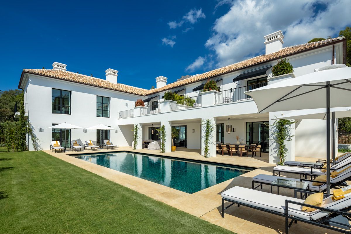 An elegant villa in Cascada de Camoján, Marbella, featuring a stunning facade with modern architectural lines, expansive glass windows, and luxurious stone accents. The villa is surrounded by lush greenery and landscaped gardens, creating a sophisticated and serene atmosphere on the prestigious Golden Mile.