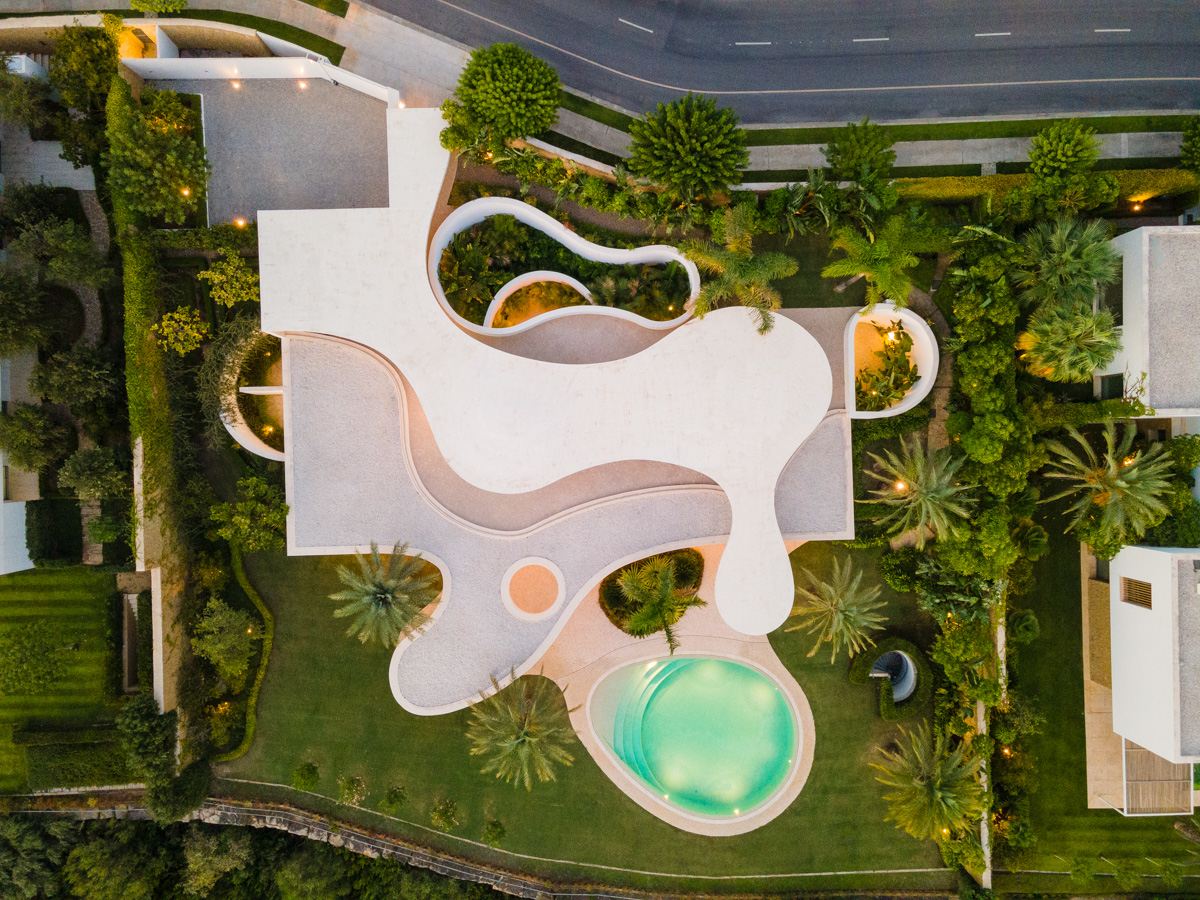 Aerial view of a futuristic villa in Finca Cortesín, Marbella, designed by Vicens Ramos, showcasing the villa's sleek, modern architecture, expansive terraces, and seamless integration with the surrounding landscape, offering panoramic views of the lush grounds and nearby golf course.