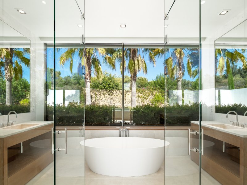 A luxurious master bathroom featuring a freestanding bathtub, a spacious walk-in shower with glass walls, and elegant marble finishes. The room is bathed in natural light from large windows, creating a serene and sophisticated spa-like atmosphere.