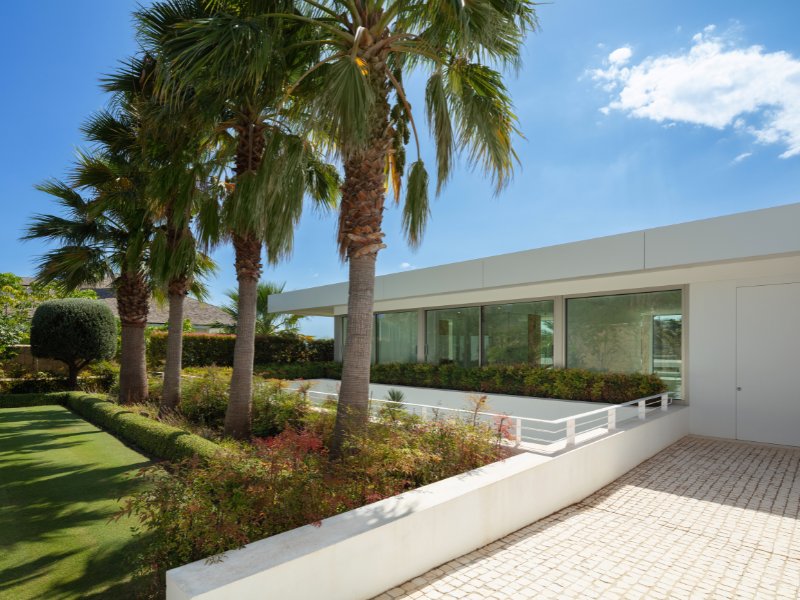 A sleek and spacious luxury villa parking area featuring a clean, modern design with soft ambient lighting. The space showcases high-end vehicles parked in an organized layout, complemented by polished flooring and contemporary architectural elements.