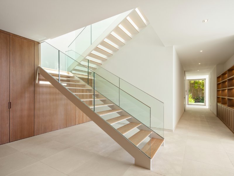 Elegant staircase in a golfside luxury villa in Finca Cortesin, featuring sleek, modern design with clean lines and high-end materials. The staircase is framed by large windows, allowing natural light to illuminate the space and offering breathtaking views of the surrounding golf course and landscape. The sophisticated design adds a sense of grandeur to the villa's interior.