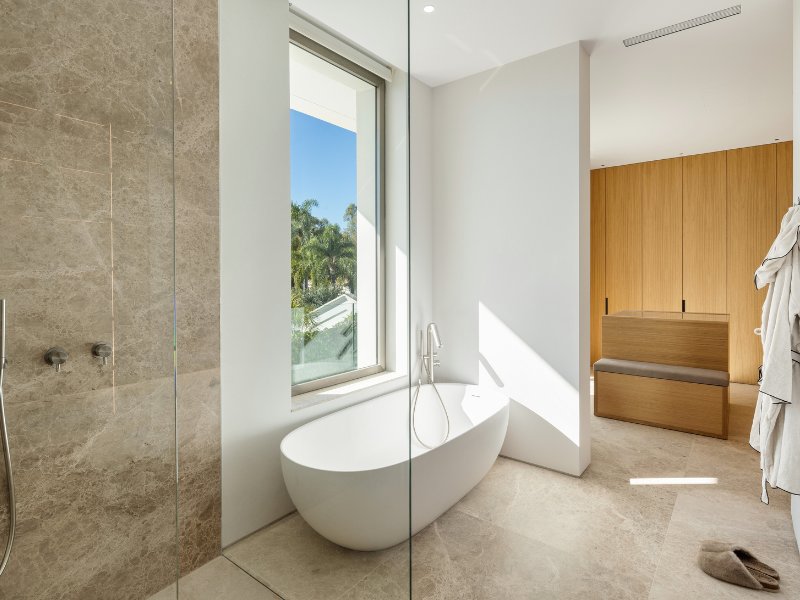 Opulent master bathroom in a luxury villa with panoramic golf and mountain views, featuring a freestanding soaking tub, sleek modern fixtures, marble finishes, and large windows that provide a serene, spa-like atmosphere with breathtaking natural surroundings.