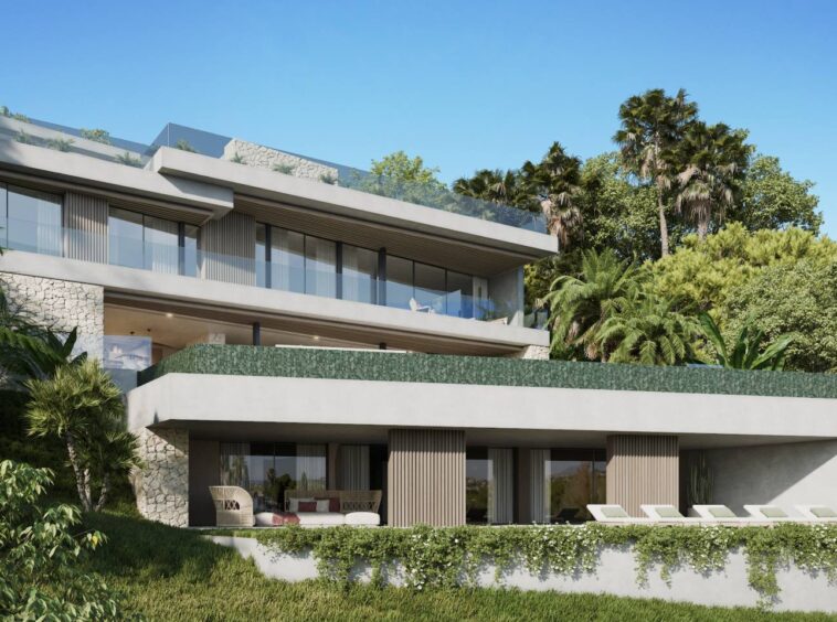 Elegant modern villa in El Herrojo, Benahavís, featuring a sleek white facade with clean architectural lines, large floor-to-ceiling windows, and warm ambient lighting. The property is surrounded by lush greenery and offers a spacious outdoor area, blending contemporary luxury with natural beauty.
