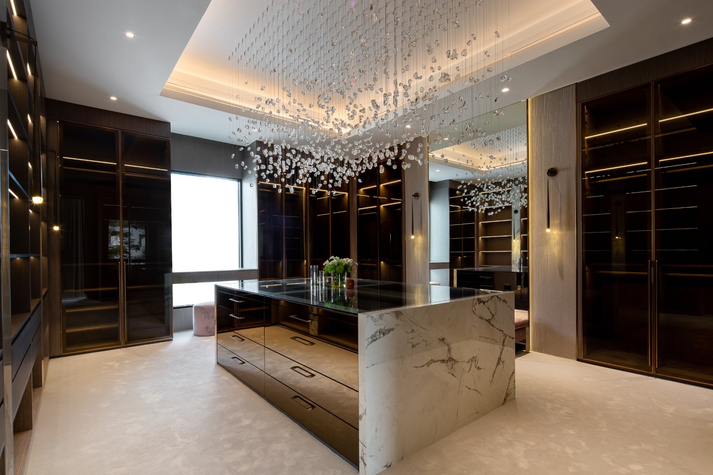 Elegant dressing room in an ultra-luxury mansion in Emirates Hills, featuring custom-built wardrobes, sleek glass doors, and soft ambient lighting. The space is designed with a modern aesthetic, offering ample storage and a sophisticated atmosphere.